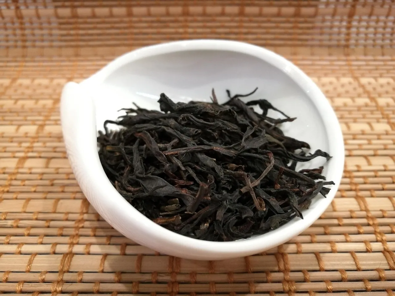 Dunkle, gedrehte Oolong-Blätter in einer weißen Porzellanschale