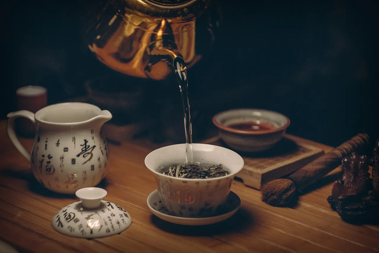 Tee wird aus einer Porzellankanne in eine kleine Tasse gegossen