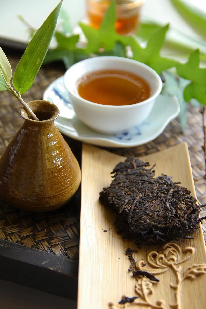 Ein Stück gepresster Pu-Erh-Teekuchen neben einer Tasse dunklen Tees
